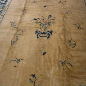 Tan low-pile rug with a blue floral vase center and wide dark blue vine border on a wood floor.