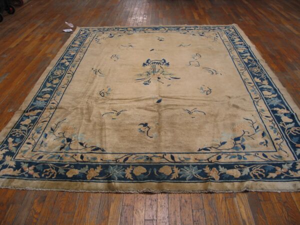 Tan field rug featuring navy blue floral borders and scattered light blue botanical designs on hardwood.