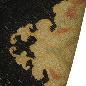 Close-up of a black, beige, and coral rug with a stylized pattern and the corner curled back.