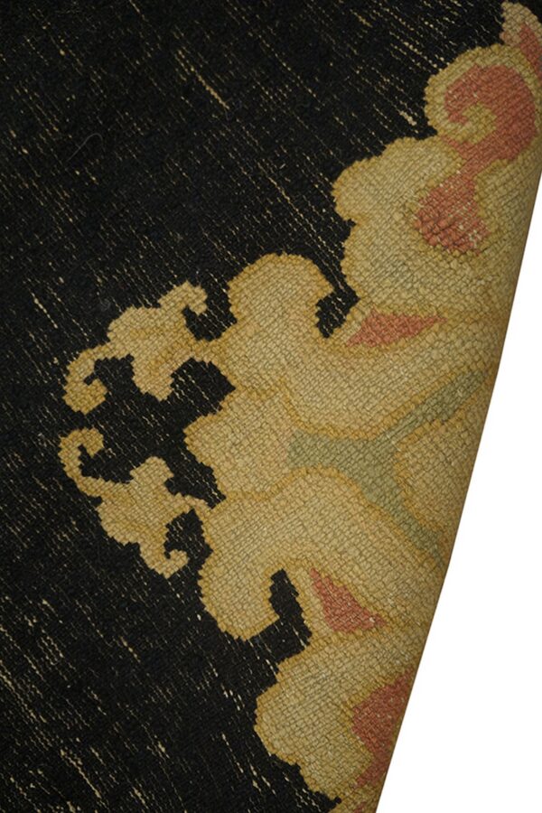 Close-up of a black, beige, and coral rug with a stylized pattern and the corner curled back.