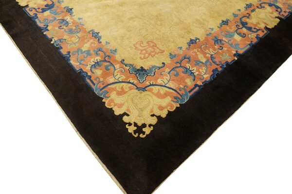 Close-up of a rug corner showing a yellow field, a peach border with blue scrolls, and a black outer edge.