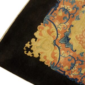 The corner of a dark-bordered rug featuring swirling blue, gold, and orange intricate floral patterns.
