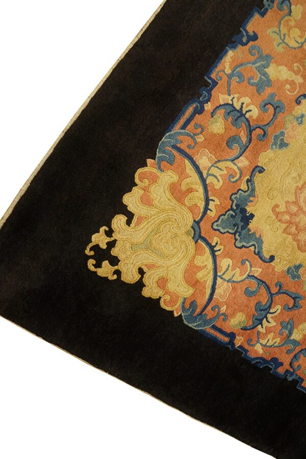 The corner of a dark-bordered rug featuring swirling blue, gold, and orange intricate floral patterns.