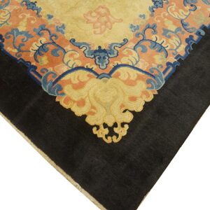 Detail of a rug corner with a black border and a complex gold, blue, and coral scrolling pattern.