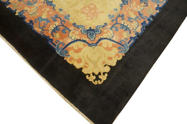 Detail of a rug corner with a black border and a complex gold, blue, and coral scrolling pattern.
