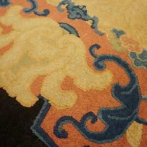 Close-up of a rug with stylized patterns in gold, burnt orange, indigo, and black.
