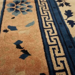 Beige field rug with blue botanical elements and a prominent blue and tan geometric key border.