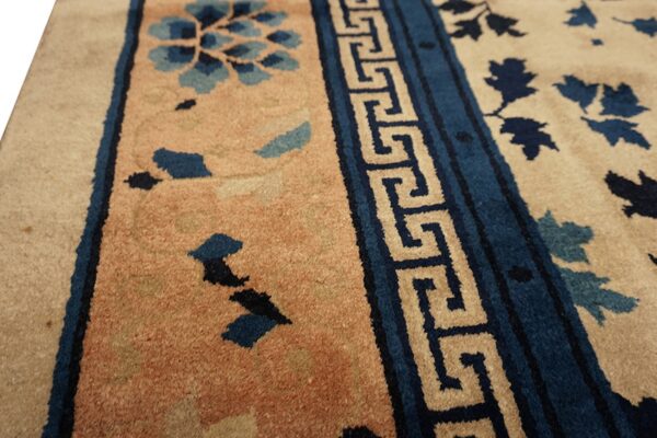 Beige field rug with blue botanical elements and a prominent blue and tan geometric key border.