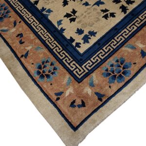 Beige rug corner featuring a complex border with deep blue geometric meander and terracotta floral medallions.