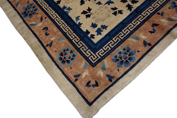 Beige rug corner featuring a complex border with deep blue geometric meander and terracotta floral medallions.