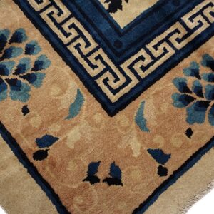 Tan field rug corner displaying blue floral clusters and a Greek key border in dark blue and beige.