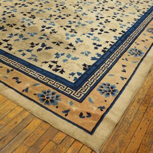 Tan rug with dark blue floral and Greek key borders rests on rustic wood flooring.