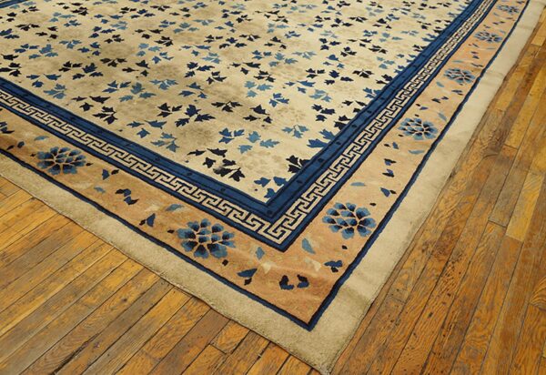 Tan rug with dark blue floral and greek key borders rests on rustic wood flooring.