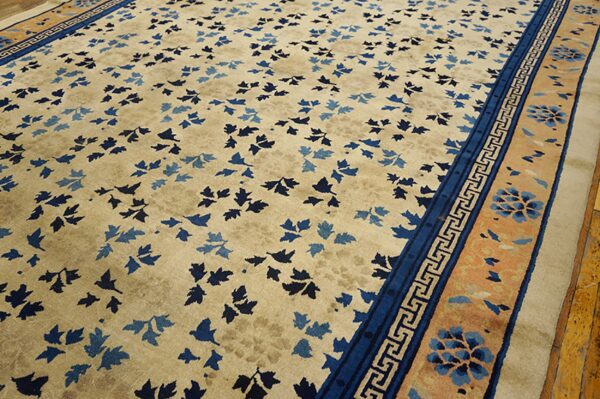 Tan rug featuring scattered blue leaves, detailed borders, lying on distressed yellow wood flooring.