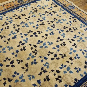 Cream field rug with scattered blue leaf motifs and a detailed blue and tan border on wood floors.