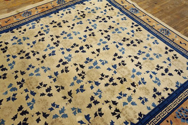 Cream field rug with scattered blue leaf motifs and a detailed blue and tan border on wood floors.