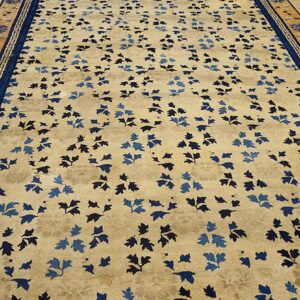 Beige rug with blue leaf pattern and intricate blue and terra cotta borders on wood flooring.