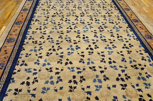 Beige rug with blue leaf pattern and intricate blue and terra cotta borders on wood flooring.