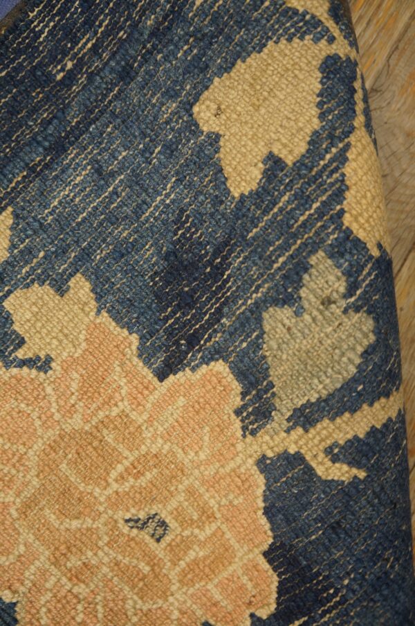 Close-up of a low-pile rug showing blue, tan, and salmon abstract floral patterns on wood planks.