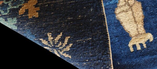 Detail of a dark blue rug with tan and light blue geometric patterns and contrasting high and low pile.