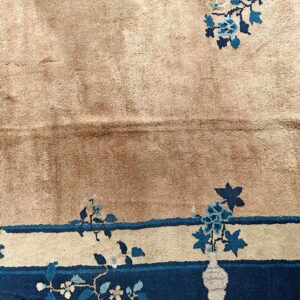 Tan rug detail shows blue floral sprays, a border stripe, and a dark blue band with a cream vase.