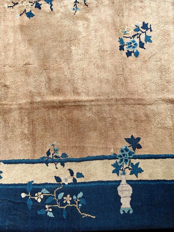 Tan rug detail shows blue floral sprays, a border stripe, and a dark blue band with a cream vase.