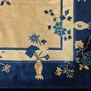 Detail of a rug showing a beige field and navy border with blue, teal, and tan botanical motifs.