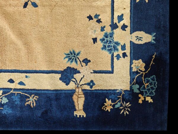 Detail of a rug showing a beige field and navy border with blue, teal, and tan botanical motifs.