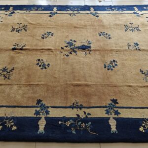 A tan rug with scattered blue floral motifs and a thick navy blue border rests on white tile.