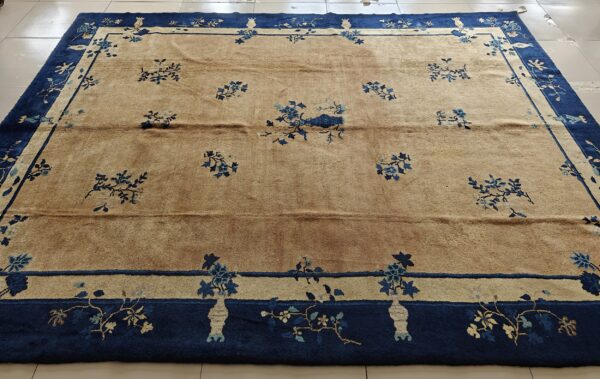 A tan rug with scattered blue floral motifs and a thick navy blue border rests on white tile.