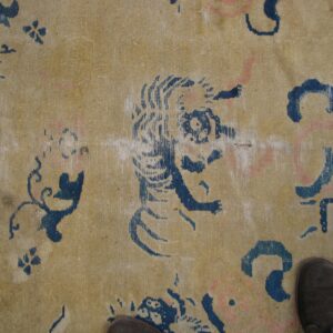 Low-pile tan rug featuring stylized indigo blue animal and floral patterns; dark shoes are visible.