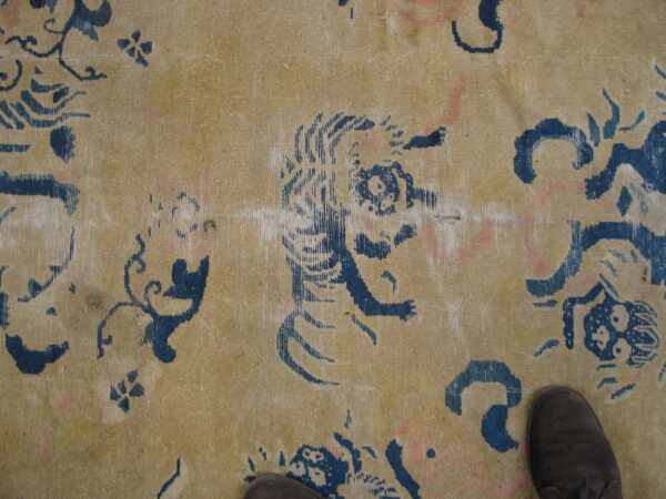 Low-pile tan rug featuring stylized indigo blue animal and floral patterns; dark shoes are visible.