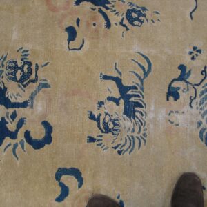 Beige rug featuring stylized indigo blue tiger patterns and faint pink details, with a brown shoe tip visible.