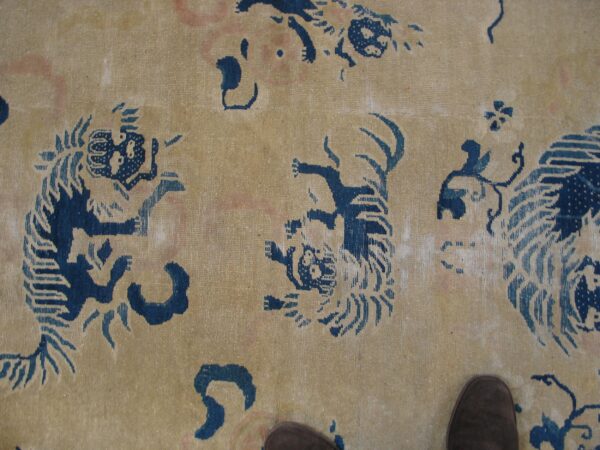 Beige rug featuring stylized indigo blue tiger patterns and faint pink details, with a brown shoe tip visible.