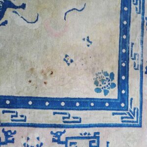 Worn cream rug with dark blue animal and floral motifs, geometric key borders, and visible staining.