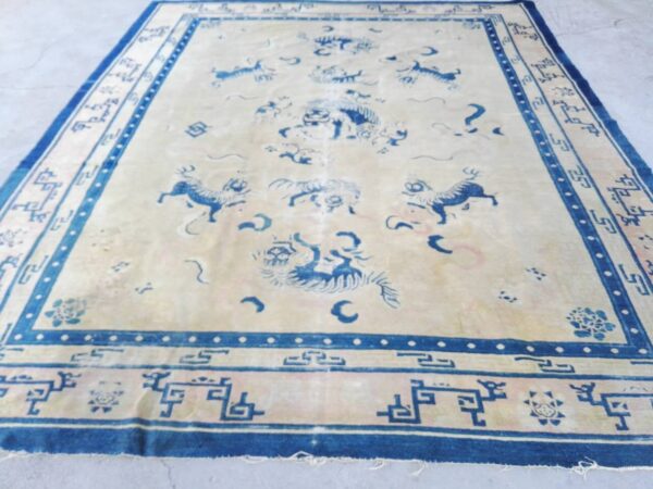Low pile rug with a cream field and deep blue borders featuring mythological creatures and geometric patterns.