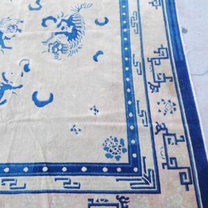 Cream and blue rug showing large stylized tiger motifs and an elaborate geometric border on a pale surface.