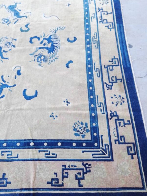 Cream and blue rug showing large stylized tiger motifs and an elaborate geometric border on a pale surface.