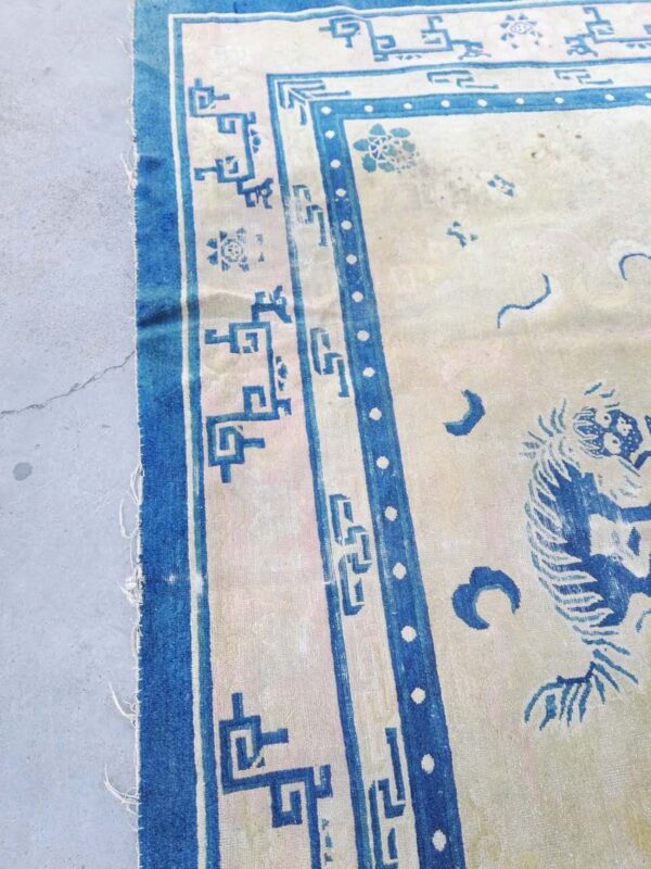 Worn beige and cobalt blue rug featuring geometric and animal patterns displayed on cracked gray concrete.
