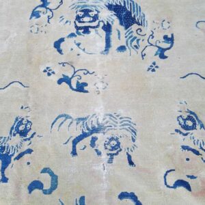 Close-up of a rug featuring blue mythological lion motifs and floral elements on a cream background.