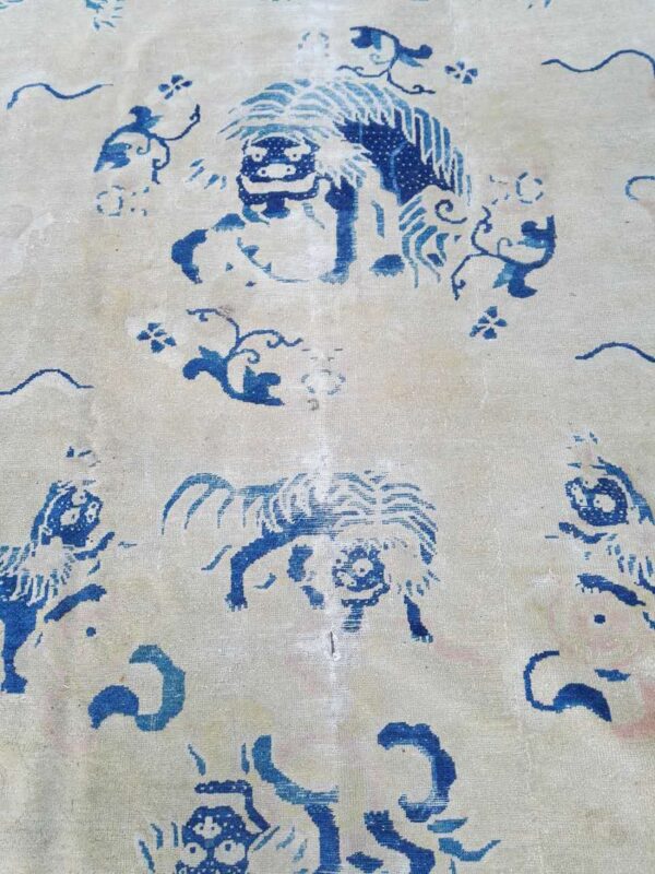 Close-up of a rug featuring blue mythological lion motifs and floral elements on a cream background.