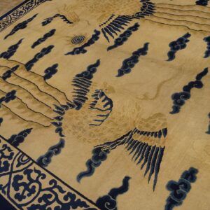 Beige rug featuring stylized gold birds and navy blue cloud motifs, bordered by dark blue scrolls on a wood floor.