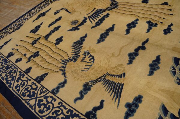 Beige rug featuring stylized gold birds and navy blue cloud motifs, bordered by dark blue scrolls on a wood floor.