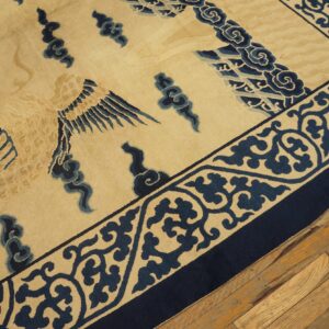 Tan rug with dark blue bird and cloud motifs and a wide, scrolled border rests on worn wood planks.