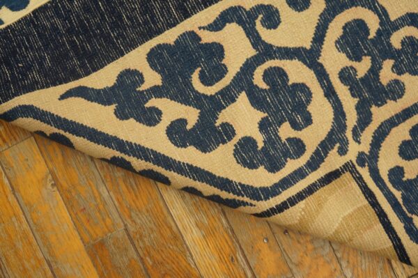 Navy blue and beige flatweave rug with a swirling pattern is partially rolled on distressed wood planks.