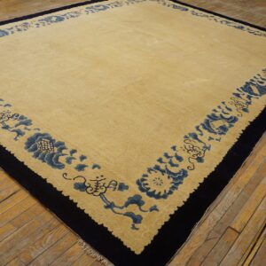 Light gold rug with a thick navy border and blue floral pattern on worn wood floors.