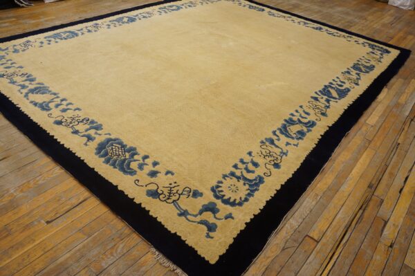 Light gold rug with a thick navy border and blue floral pattern on worn wood floors.