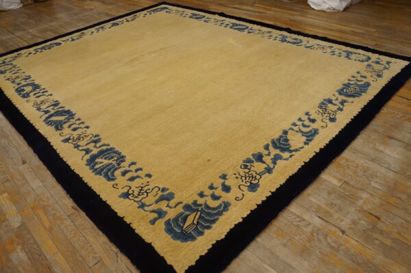 Tan rug with a wide dark blue stylized border and solid navy edge rests on wooden plank flooring.