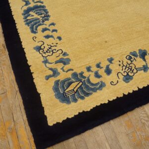 Gold pile rug with a navy border and blue scalloped design lies on worn wooden flooring.