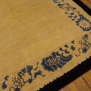 Gold rug with a medium pile features a dark blue floral and black border on wood flooring.